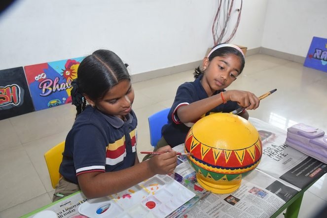Two students painting a decorated pot during an art session