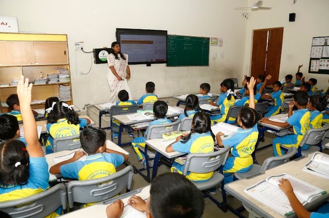 A teacher leading a lesson on the smart classroom display as students raise their hands